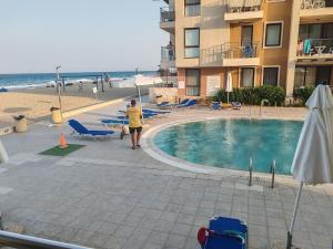 a woman standing next to a swimming pool next to a beach at Апартамент E003 в Обзор Бийч Резорт - усещането да живееш на плажа!! in Obzor