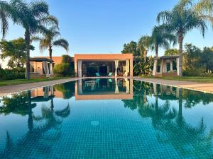 a swimming pool in front of a house with palm trees at Villa Serenity Marrakech in Châba