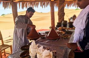 a man standing at a table in the desert at mhamid luxury camps 