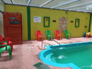 a swimming pool with red and green chairs in a room at Departamentos Mon in San Clemente del Tuyú