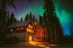 una baita sotto l'aurora boreale nel bosco di notte di Experience Lakeside Cabin Living in North Pole, AK a North Pole