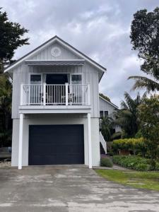 a white house with a balcony and a garage at The Boat House Studio in Tairua
