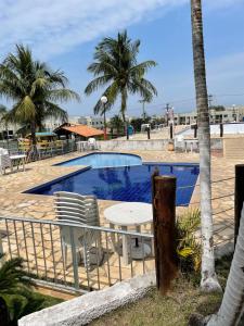 a swimming pool with a table and chairs and palm trees at Comfort and good memories, right by the lagoon! in São Pedro da Aldeia