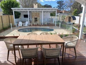 a wooden table and chairs on a deck with a pool at Bluebell Huskisson in Huskisson