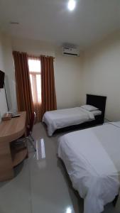 a hotel room with two beds and a desk and a window at Hotel Prasasti Pacitan in Pacitan