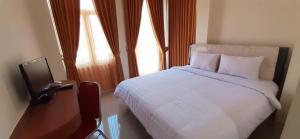 a bedroom with a white bed and a television at Hotel Prasasti Pacitan in Pacitan