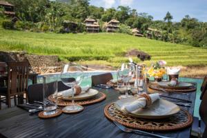 a wooden table with glasses and plates on it with a field at Pu Luong EcoLuxe Resort & Spa in Lũng Tiềm