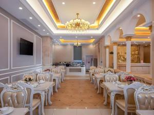 une salle de banquet avec des tables et des chaises blanches et un lustre dans l'établissement Vienna Hotel Yueyang East Station, à Yueyang