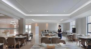 a man standing in a room with tables and chairs at Vienna Hotel Zhejiang Tongxiang Puyuan in Jiaxing