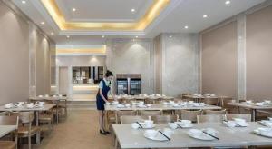 a woman standing in a dining room with tables at Vienna Hotel Fuzhou Changle Shouzhan Hangcheng Metro Station in Fuzhou