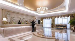 永川Vienna Hotel Chongqing Yongchuan High-Speed Railway Station Xinglong Lake的一名持行李站在酒店大堂的男子