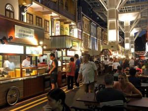 Un grupo de personas de pie alrededor de un patio de comidas en un restaurante. en Royal Hostel Singapore, en Singapur