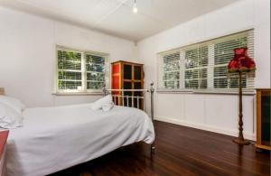 a white bedroom with a bed and two windows at Frankies Beach House - 1 A Carlyle Lane in Byron Bay