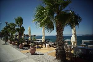 a patio with tables and chairs and palm trees and the ocean at Valis Resort Hotel in Volos