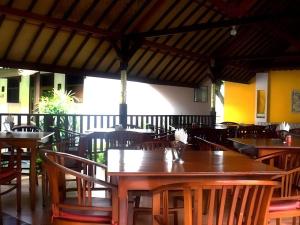 an empty restaurant with wooden tables and chairs at Hotel Ratih in Gili Trawangan