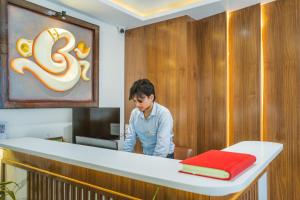a man standing behind a counter with a red towel at Tripli Hotels Sandalwood in Varanasi