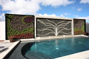 a swimming pool in front of a wall with a garden at HS HOTSSON Hotel Queretaro in Querétaro