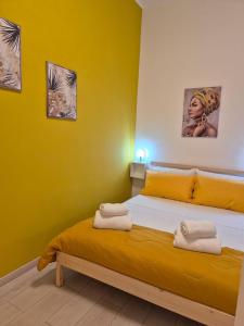a bedroom with yellow walls and a bed with towels on it at House Mari in Catania