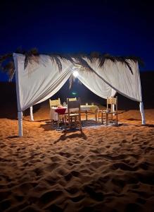 a table and chairs under a white canopy on the beach at Merzouga Standard Bivouac in Merzouga