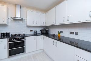a white kitchen with white cabinets and black appliances at Open Mind Property - 3 Bed Home with Free Parking in Portsmouth