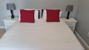 a white bed with two red pillows on it at December Holiday Home George in George