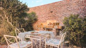 a patio with a table and chairs and a brick wall at Hitgeheim Garden Cottages in Addo