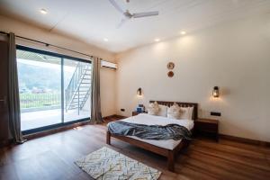 a bedroom with a bed and a large window at SaffronStays Pebble House - 3BR riverside villa with glass walls, terraces & Nun River views, Dehradun in Dehradun