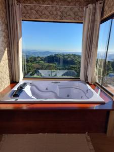 a bath tub in a room with a large window at Chalés Ser Tão di Minas in Paraisópolis