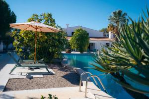 a pool with an umbrella and chairs next to a house at Quinta do Vale Entire Property in São Bartolomeu de Messines