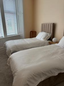 two beds in a bedroom with white sheets at Crescent Corner 44 Seamore Str Ground Floor Right in Largs