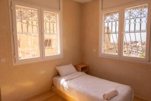 a small bedroom with a bed and two windows at Surf & bask HOME in Tamraght Ouzdar