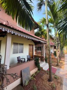 a house with a porch with chairs and palm trees at Leela Grove Cottages Gokarna in Gokarna