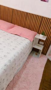 a bedroom with a bed with a pink pillow and a side table at Quartos Privados em casa Mobiliada in Londrina