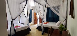 two beds in a room with curtains and a table at Nionje Garden Villa in Jambiani