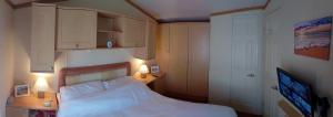 a small bedroom with a bed and a desk and cabinets at Caravan Cariad in Llangrannog