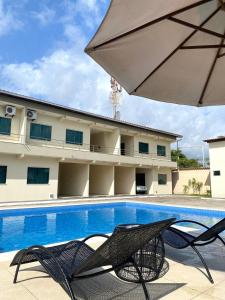 a hotel with a swimming pool with chairs and an umbrella at Cacao's Guaibim Residence in Valença