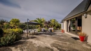 un patio avec tables, chaises et un parasol dans l'établissement la villa des temps modernes, à Trégastel
