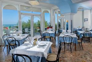 a dining room with white tables and chairs and windows at Strand Hotel in Gabicce Mare