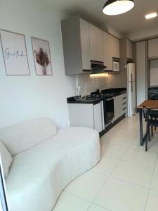 a living room with a white couch and a kitchen at Apartamento novo, 2 quartos a 50 metros da praia in Palhoça