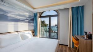 Un dormitorio con una cama y una ventana grande. en Floral Hotel Qingdao Dreamship Seaview Hotel, en Qingdao