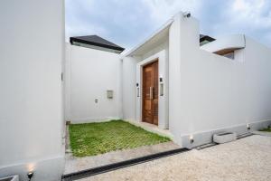 a white house with a wooden door and grass at Casa Santisya 4 by Orivista , 4min beach in Mengwi