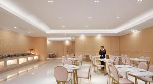a woman standing in a restaurant with tables and chairs at Vienna Hotel Shanghai Hongqiao Hub National Exhibition Center Huqingping Road in Shanghai