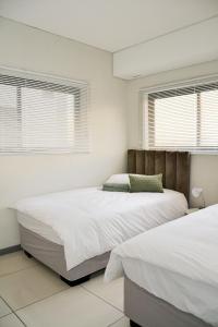 two beds in a bedroom with white walls and windows at Platinum Heights Merensky in Windhoek