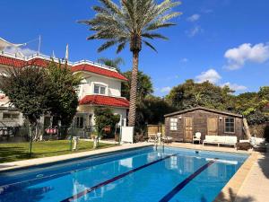 a swimming pool in front of a house with a palm tree at Sleeps 12 Family Villa By The Sea W Jacuzzi & Pool in Jisr ez Zarqā