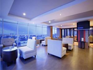 una sala de estar con sillas blancas, mesas y ventanas en Hotel Santika Makassar, en Makassar