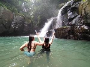 two women in the water in front of a waterfall at La Ceiba Biolgical Reserve in Platanillo