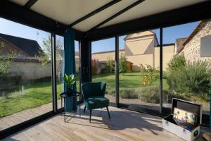 ein Wohnzimmer mit großen Fenstern und einem grünen Stuhl in der Unterkunft Le Relais d'Ezy - 3 chambres in Ézy-sur-Eure