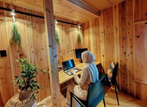 a woman sitting at a desk with a laptop in a wooden room at Kaido Yuzawa Onsen Hostel in Yuzawa