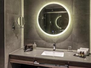 a bathroom with a sink and a round mirror at Pullman Santiago El Bosque in Santiago +140 photos