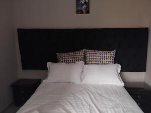 a bed with a black headboard and white sheets and pillows at Dacaso Apartments in Solwezi